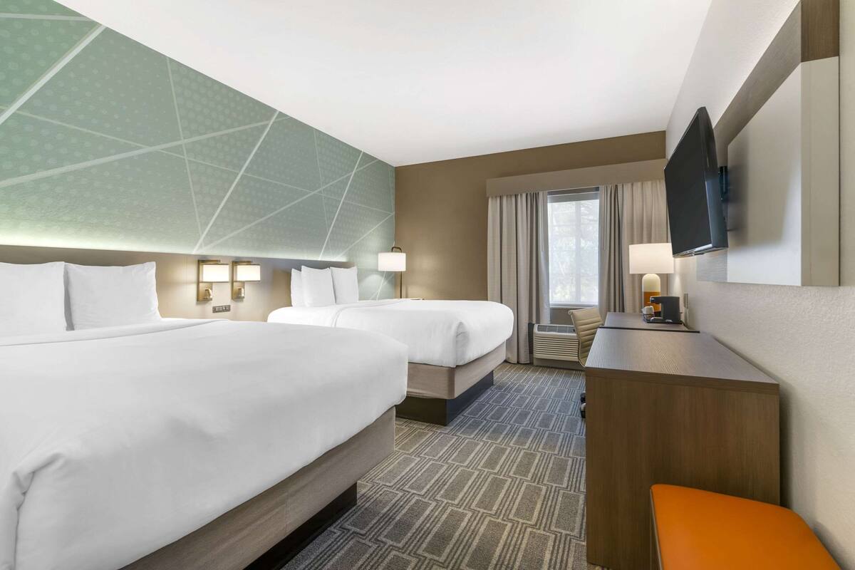 A hotel room with two beds, a desk, a TV, and a window with curtains.