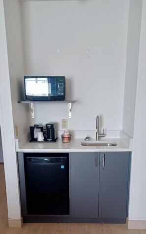 Een kleine keuken met een magnetron, koffiezetapparaat en spoelbak.