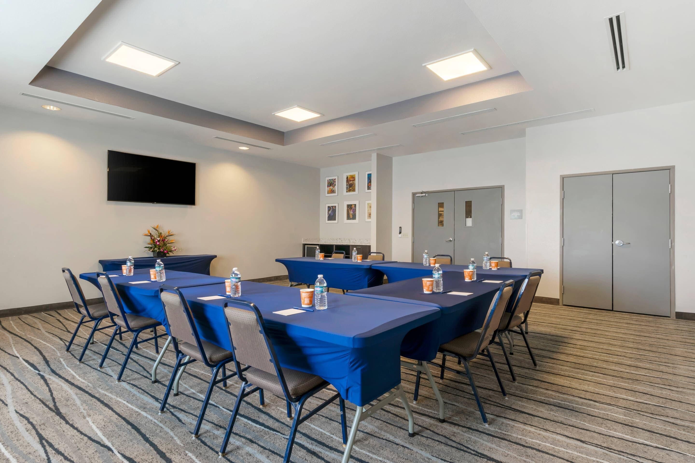 A conference room with tables and chairs, a flat-screen TV, and a door.