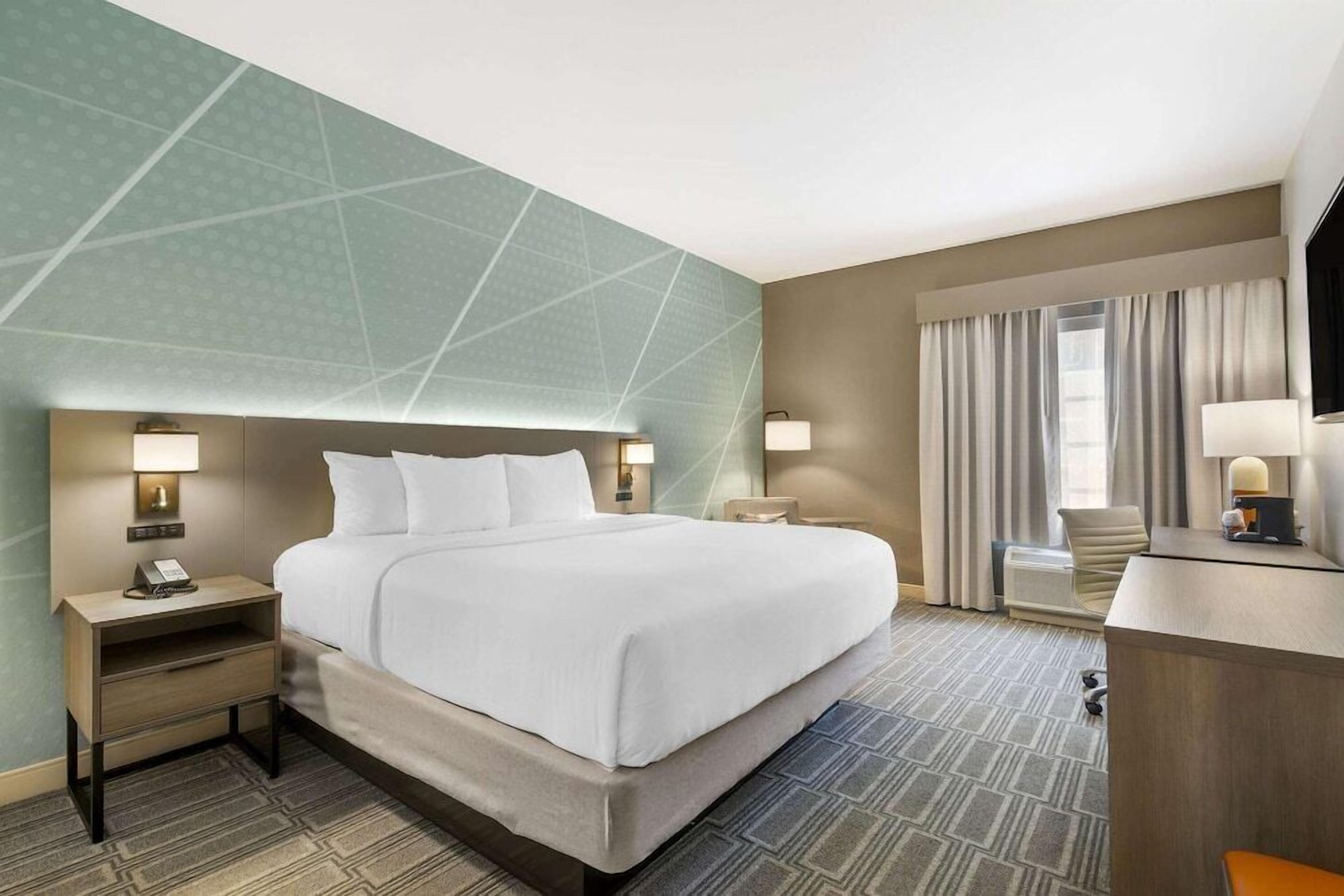A hotel room with a large bed, two bedside tables with lamps, a desk, and a chair.