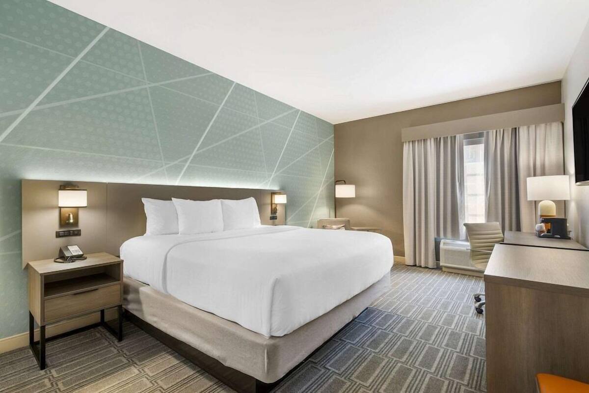 A hotel room with a large bed, two bedside tables with lamps, a desk, and a chair.