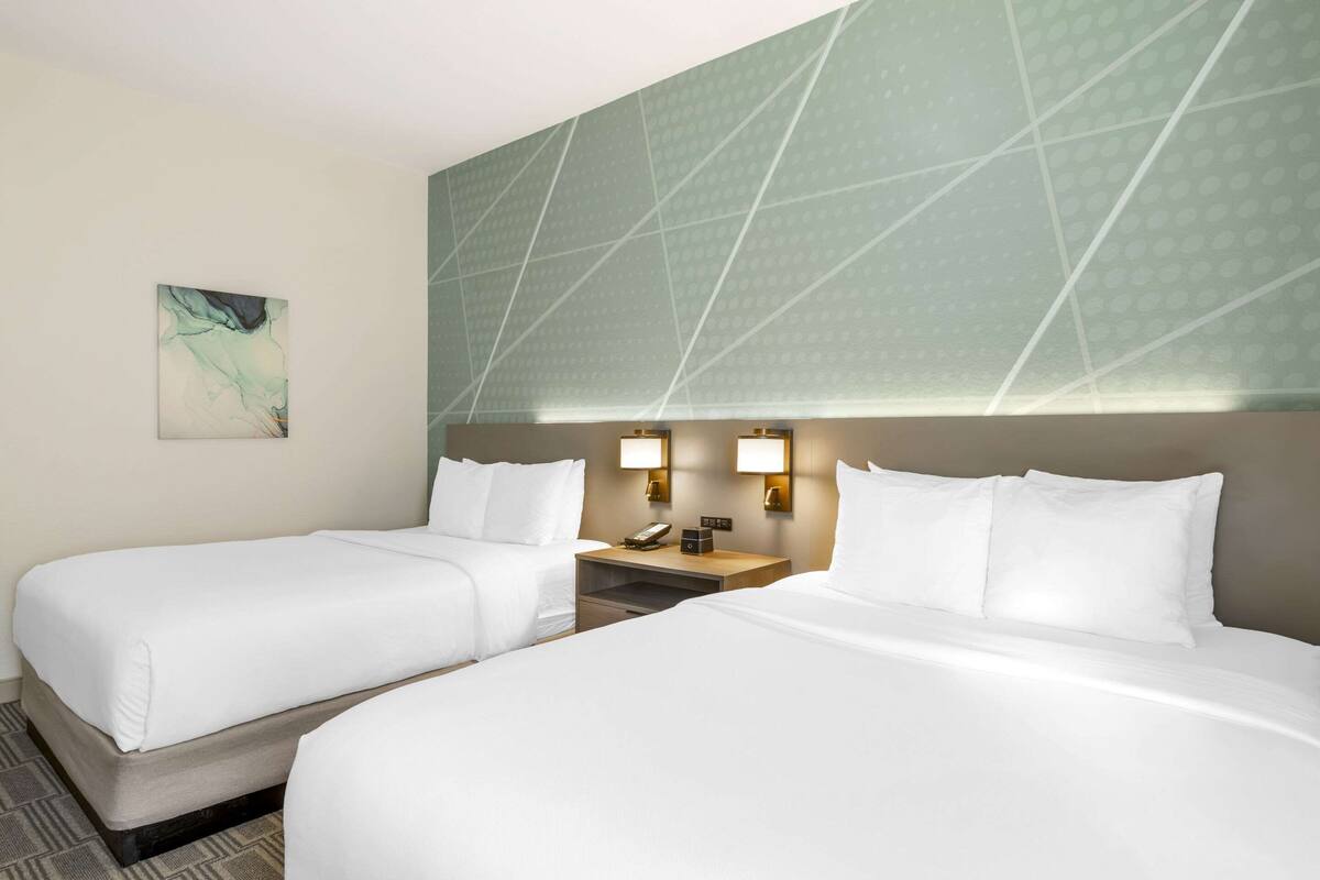 A hotel room with two beds, a nightstand, and a wall-mounted light fixture.