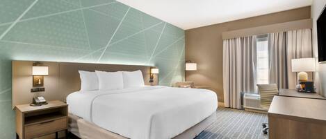A hotel room with a large bed, bedside tables with lamps, a desk with a chair, and a large window with curtains.