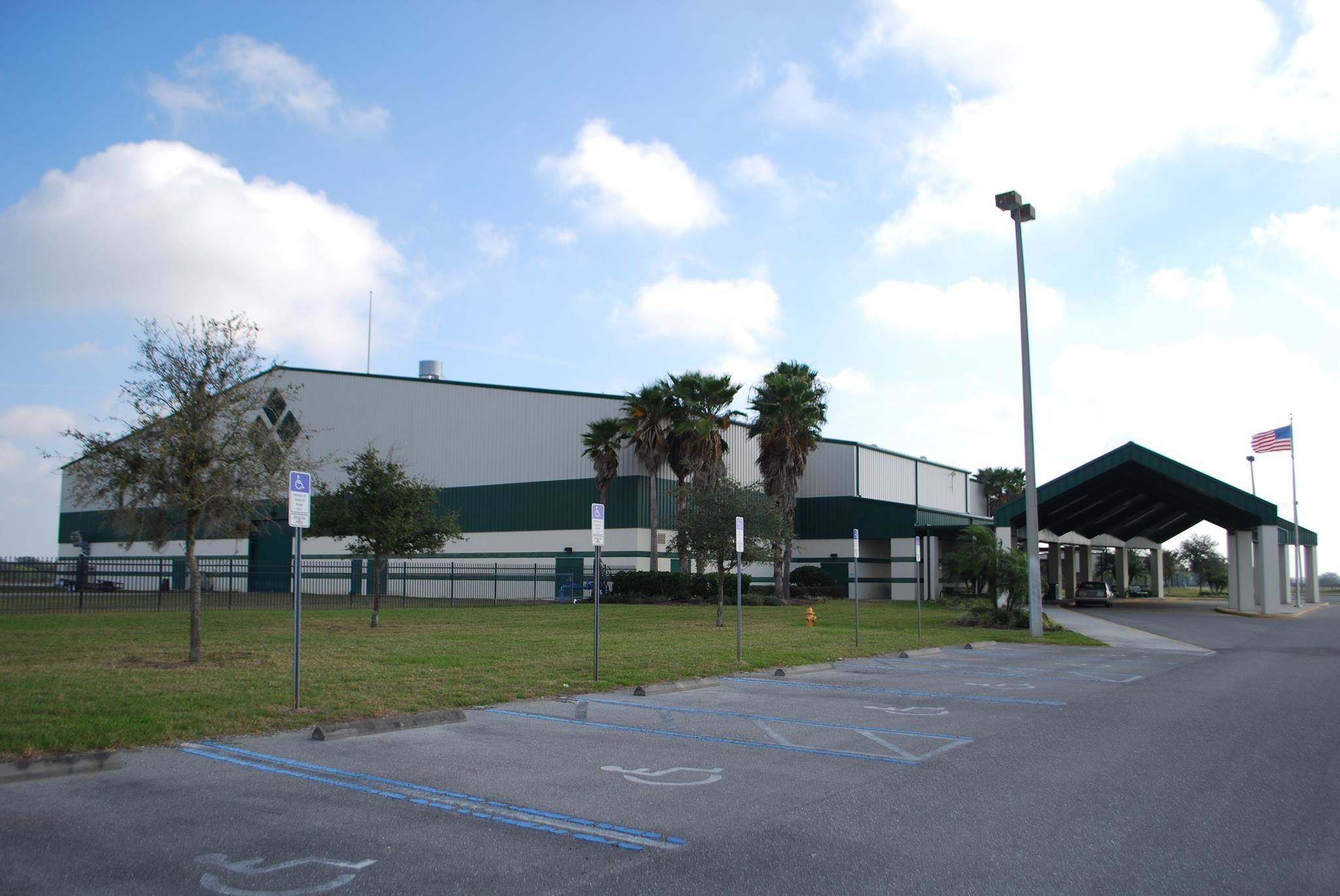 A large building with a parking lot, a covered entrance, and a flag.