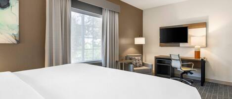 Una habitación de hotel con una cama grande, un escritorio con silla, un televisor y una ventana con cortinas.