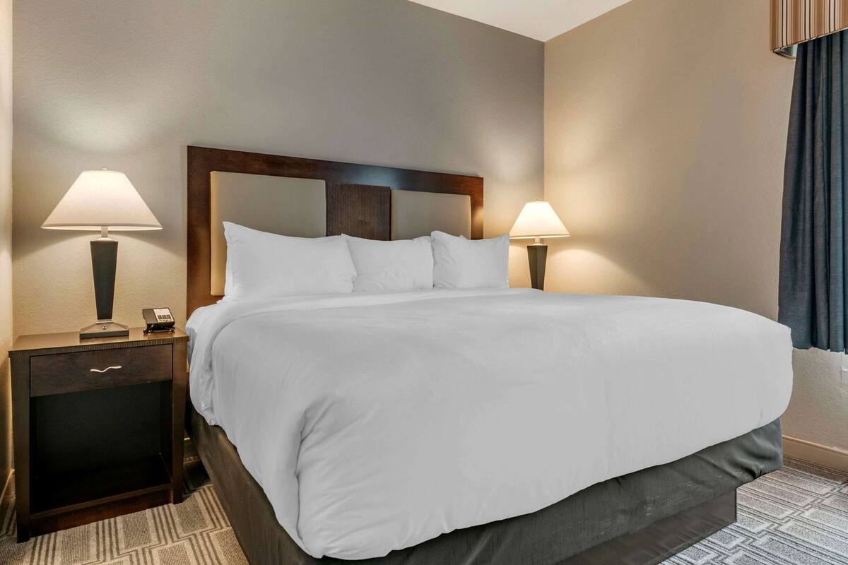 A hotel room with a large bed, two bedside tables with lamps, a wooden headboard, and a carpeted floor.