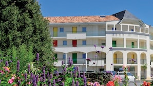 A multi-story building with balconies, a tiled roof, and a garden with purple flowers. - Résidence Les Jardins de l'Amirauté - Vacancéole (Les Sables-d'Olonne)