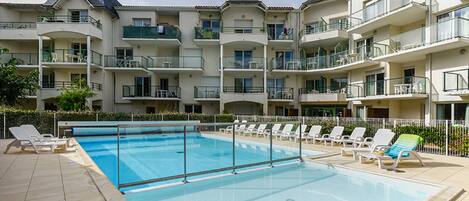 Une piscine entourée de chaises longues, elle-même bordée d’immeubles résidentiels à plusieurs étages dotés de balcons.