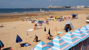 A beach with colorful umbrellas, beach chairs, and a lifeguard tower. - Résidence Les Jardins de l'Amirauté - Vacancéole (Les Sables-d'Olonne)