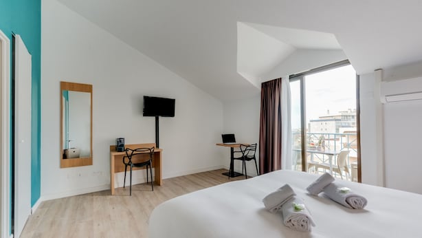 Habitación de hotel moderna con una cama grande, un escritorio, una silla, un televisor y vistas de la ciudad por la ventana.