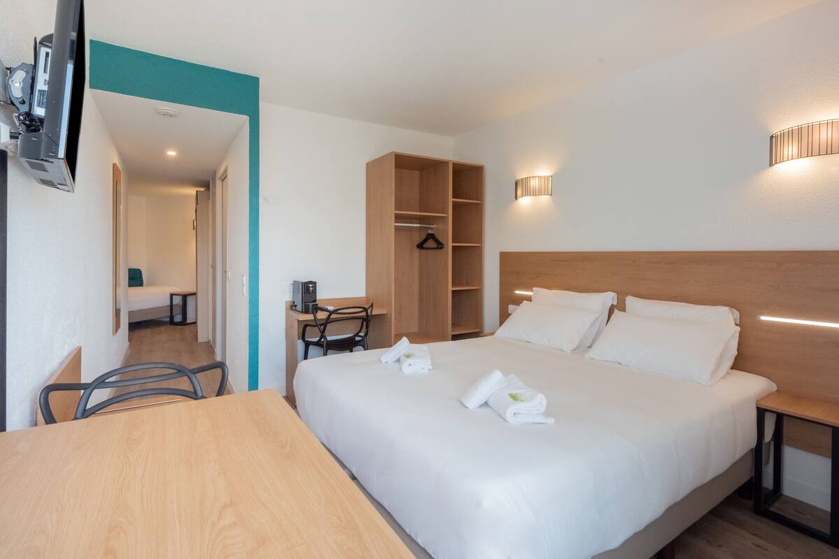 Une chambre d’hôtel équipée d’un lit, d’un bureau, d’une chaise, d’une armoire et d’un téléviseur fixé au mur.