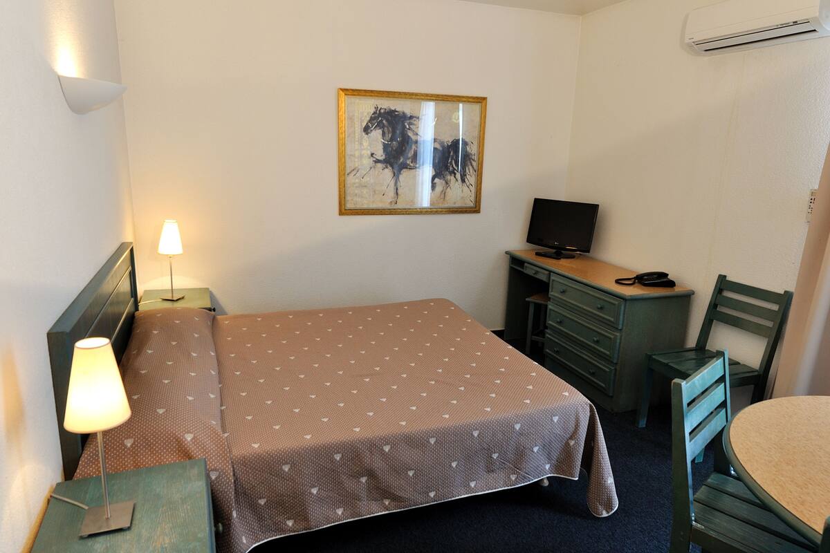 Une chambre d’hôtel avec un lit, une lampe de chevet, un bureau avec un ordinateur, une chaise et un tableau au mur.
