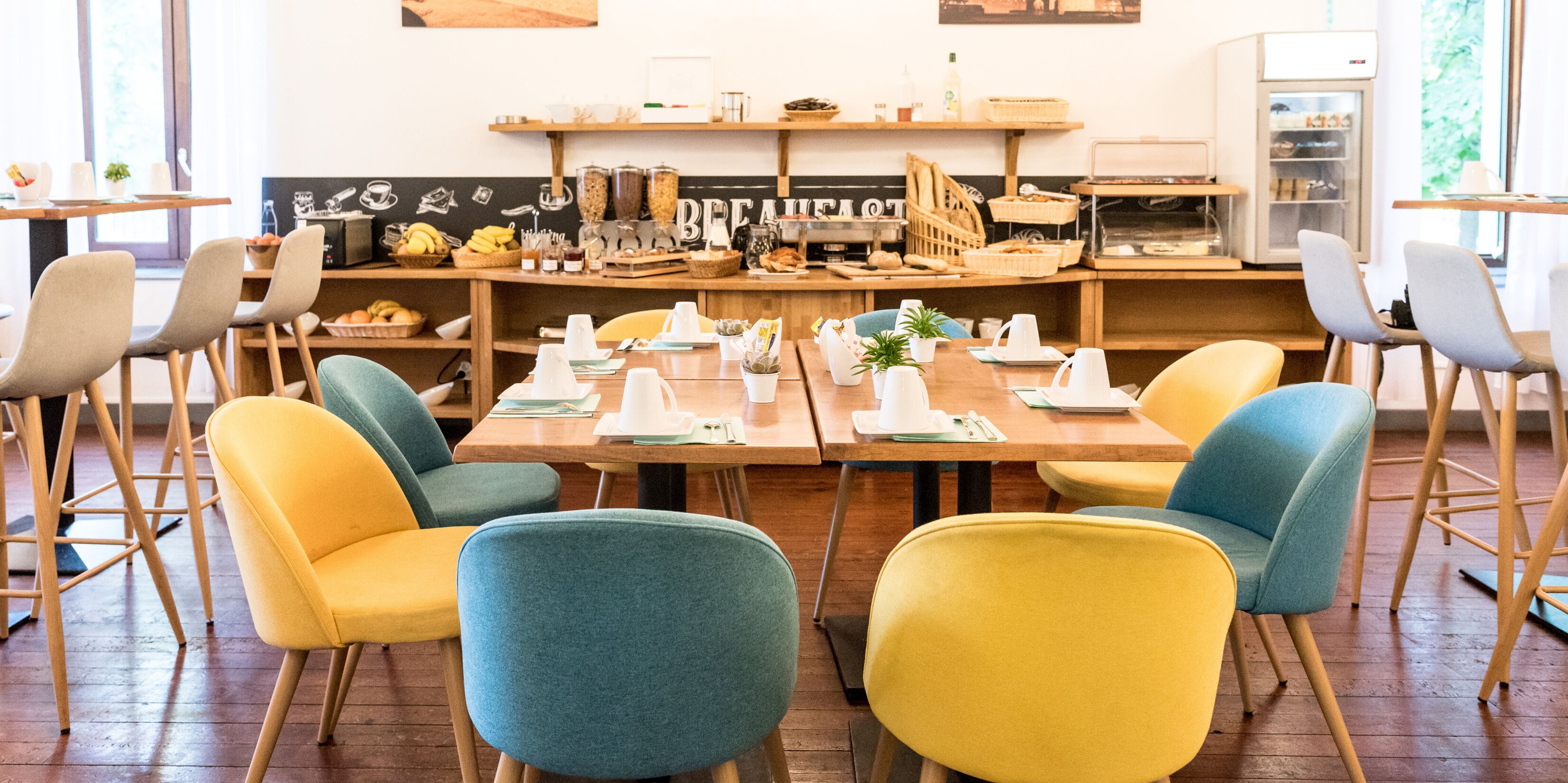 Un espace dédié au petit-déjeuner, avec des tables en bois, des chaises colorées et une variété d’aliments présentés pour le petit-déjeuner.
