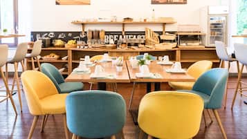 Un espace dédié au petit-déjeuner, avec des tables en bois, des chaises colorées et une variété d’aliments présentés pour le petit-déjeuner.