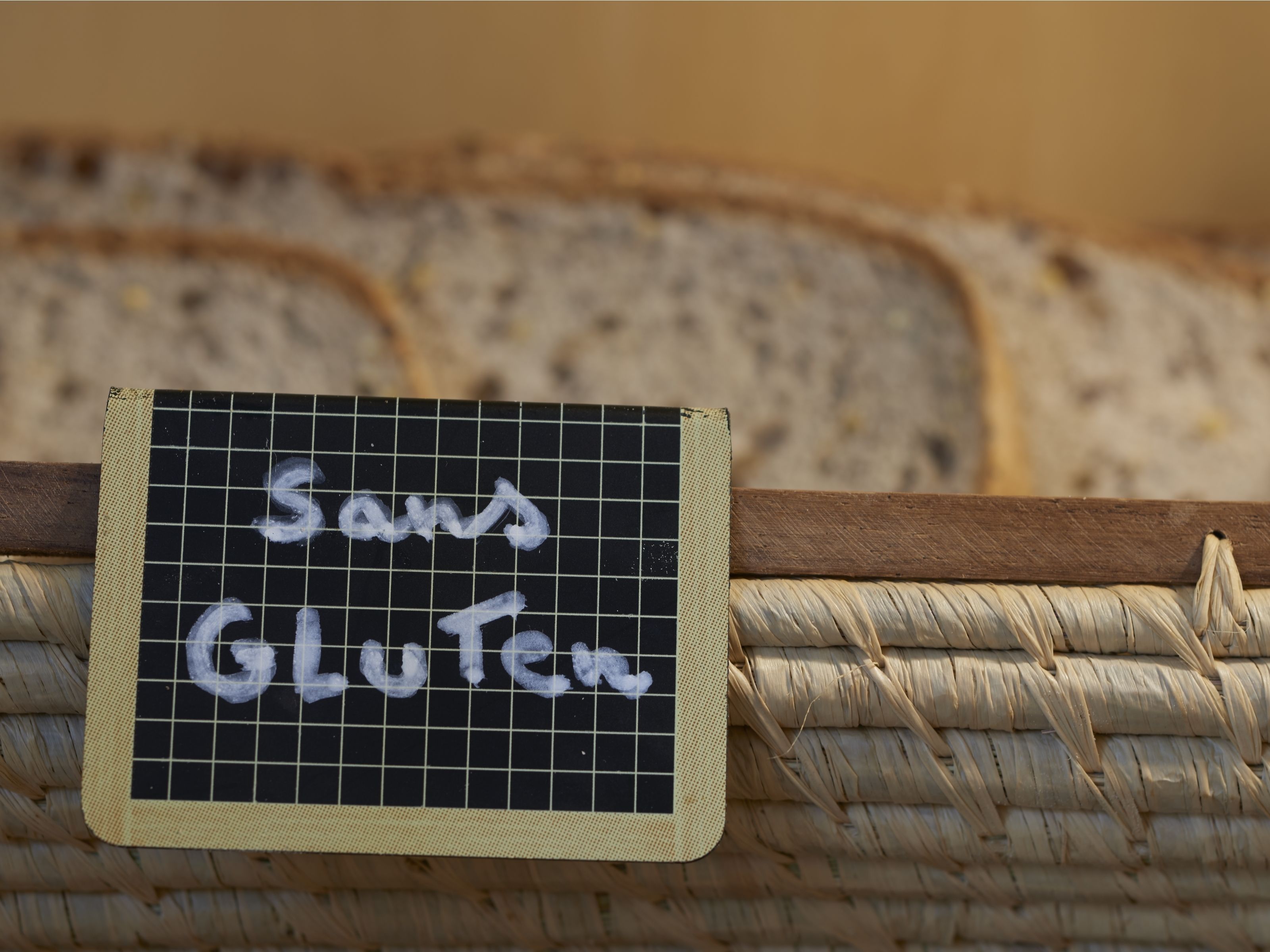 Eine Tafel mit dem Schriftzug 'Sands Gluten' auf kariertem Hintergrund, platziert in einem gewebten Korb.