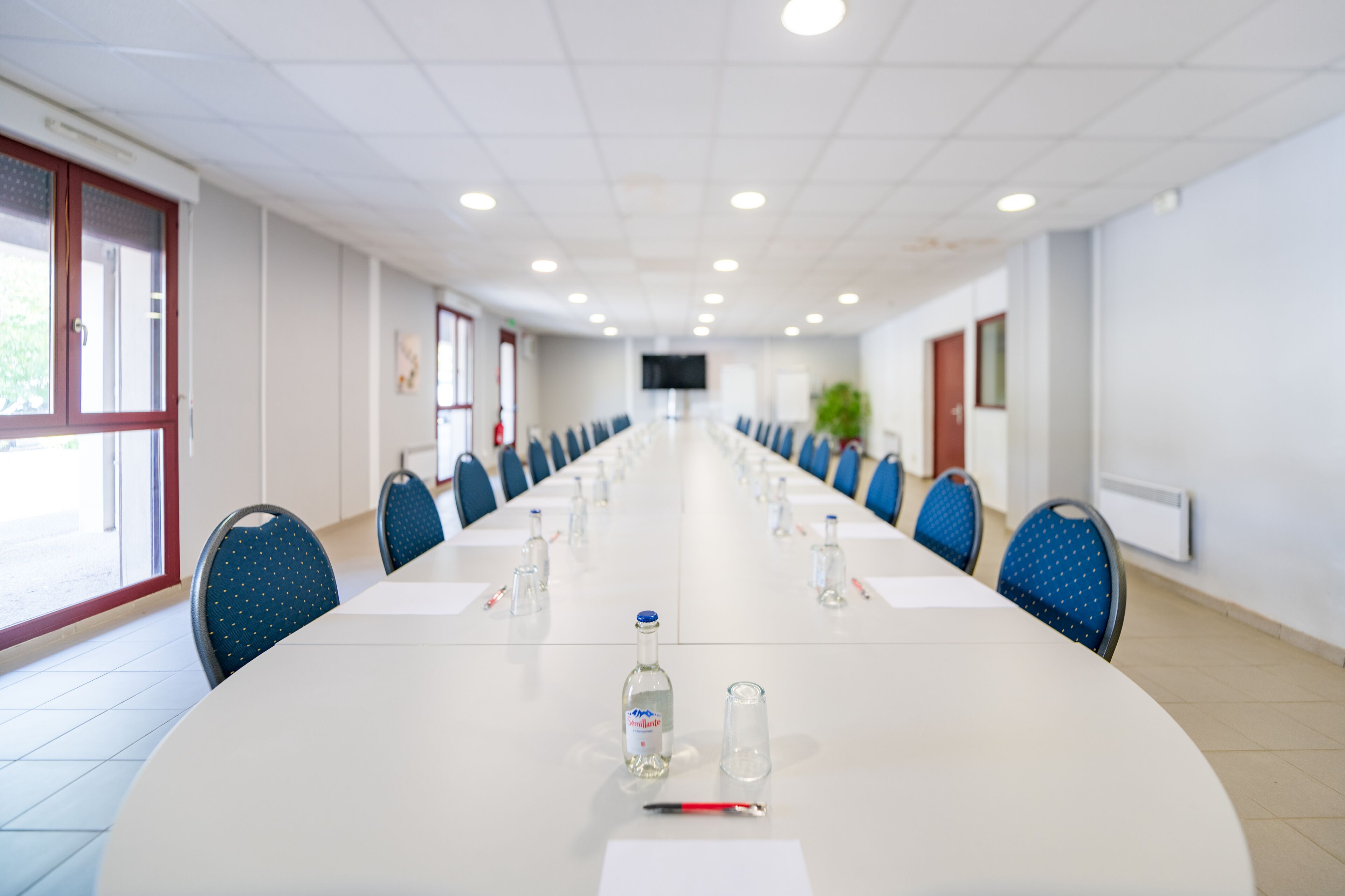 A conference room with a long table, chairs, and a projector screen.