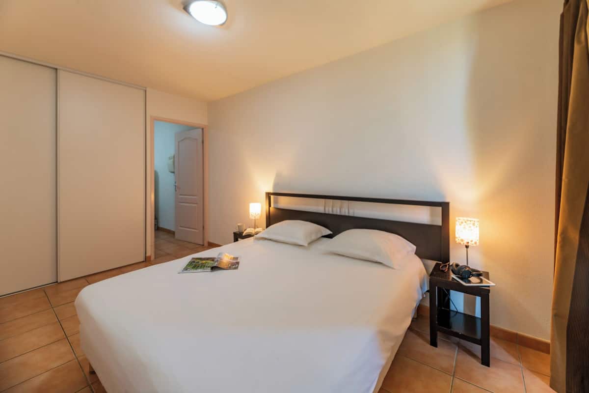 Ein Hotelzimmer mit einem großen Bett, zwei Nachttischlampen, einem Nachttisch und einer Tür zu einem weiteren Raum.