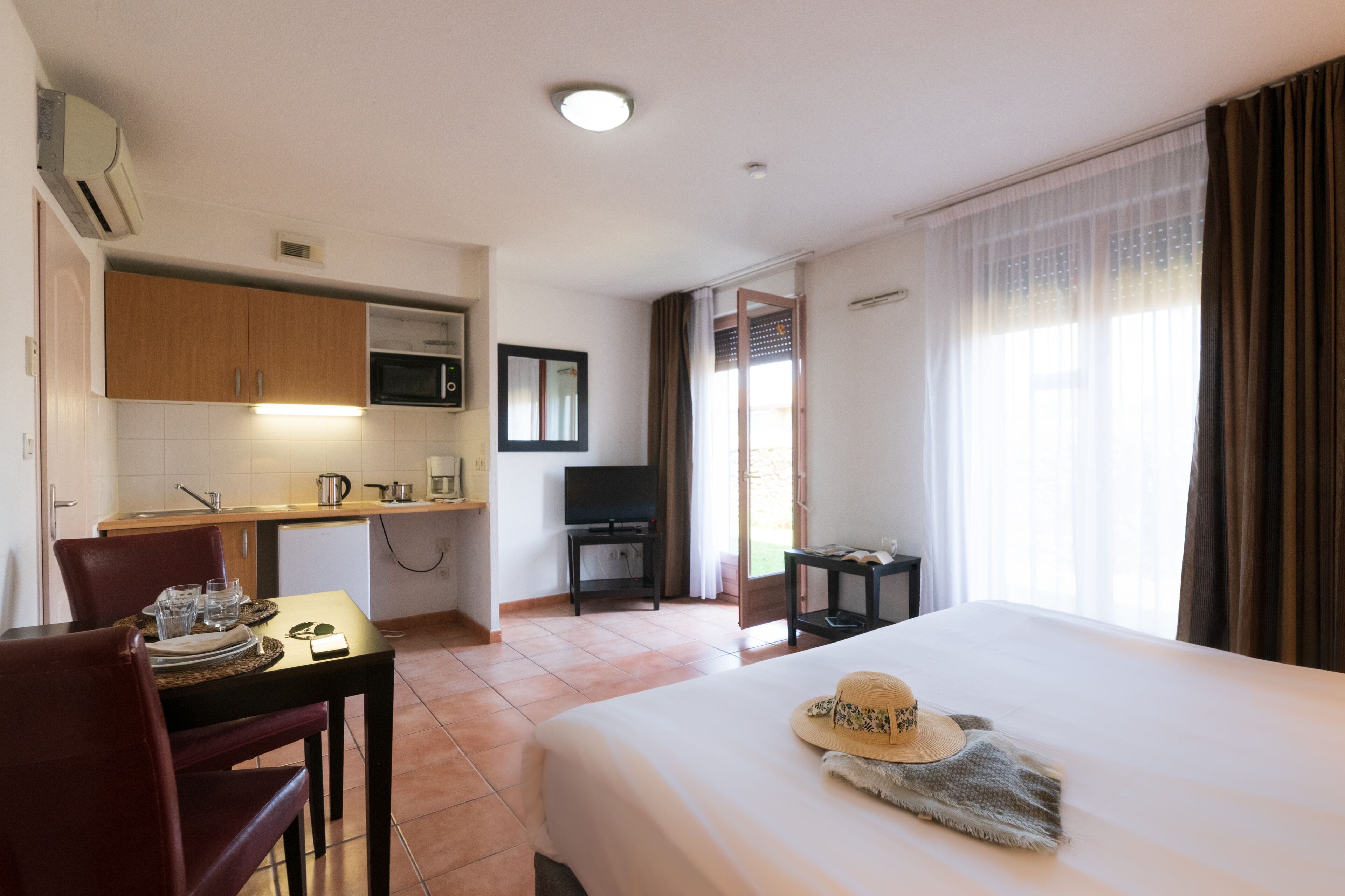 Una habitación de hotel con cama, una mesa de comedor con sillas, una zona de cocina con microondas y un televisor.