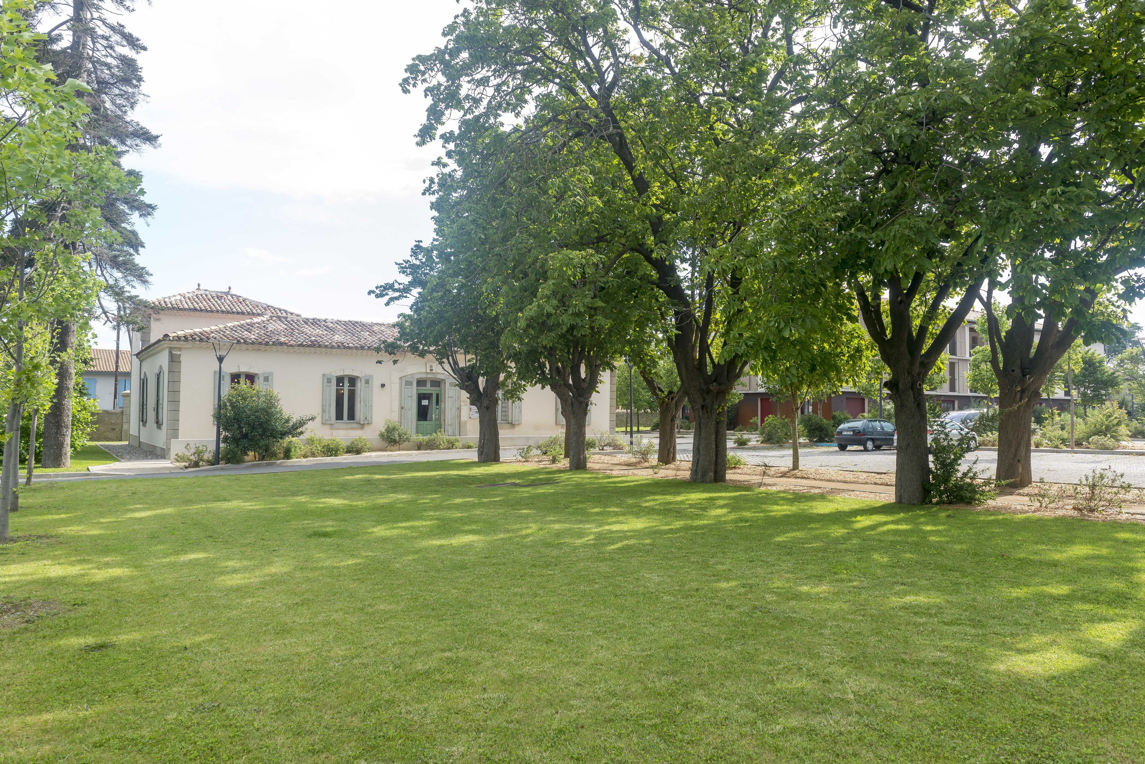 A residential property with a well-maintained lawn, mature trees, and a building with a tiled roof.