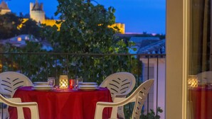 Mesa para dos con mantel rojo, sillas blancas y una vista de un castillo al fondo.