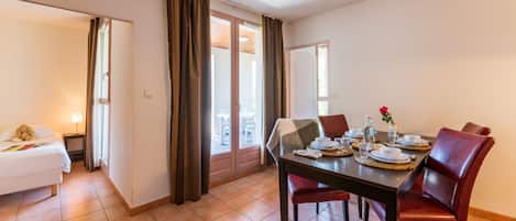 A hotel room with a dining area featuring a table set for four, a bed, and a view through a sliding door.