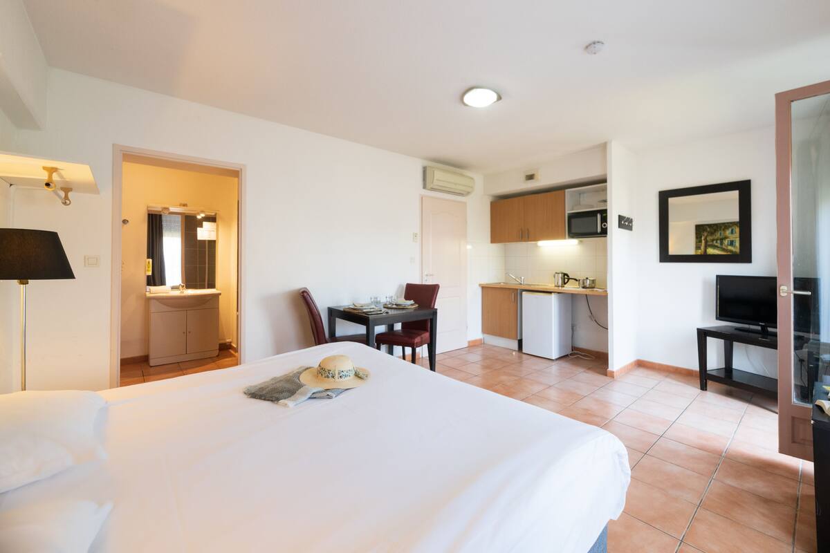 Ein Hotelzimmer mit Bett, Esstisch, Stuhl, Fernseher und einer Küchenzeile.