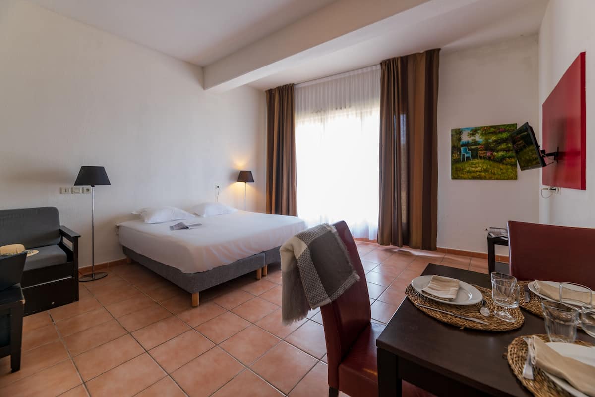 Ein Hotelzimmer mit Bett, Schreibtisch, Stuhl, Lampe, gedecktem Tisch und einem Gemälde an der Wand.