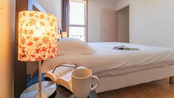 Une chambre d’hôtel avec un lit, une table de chevet avec une lampe, un livre et une tasse.