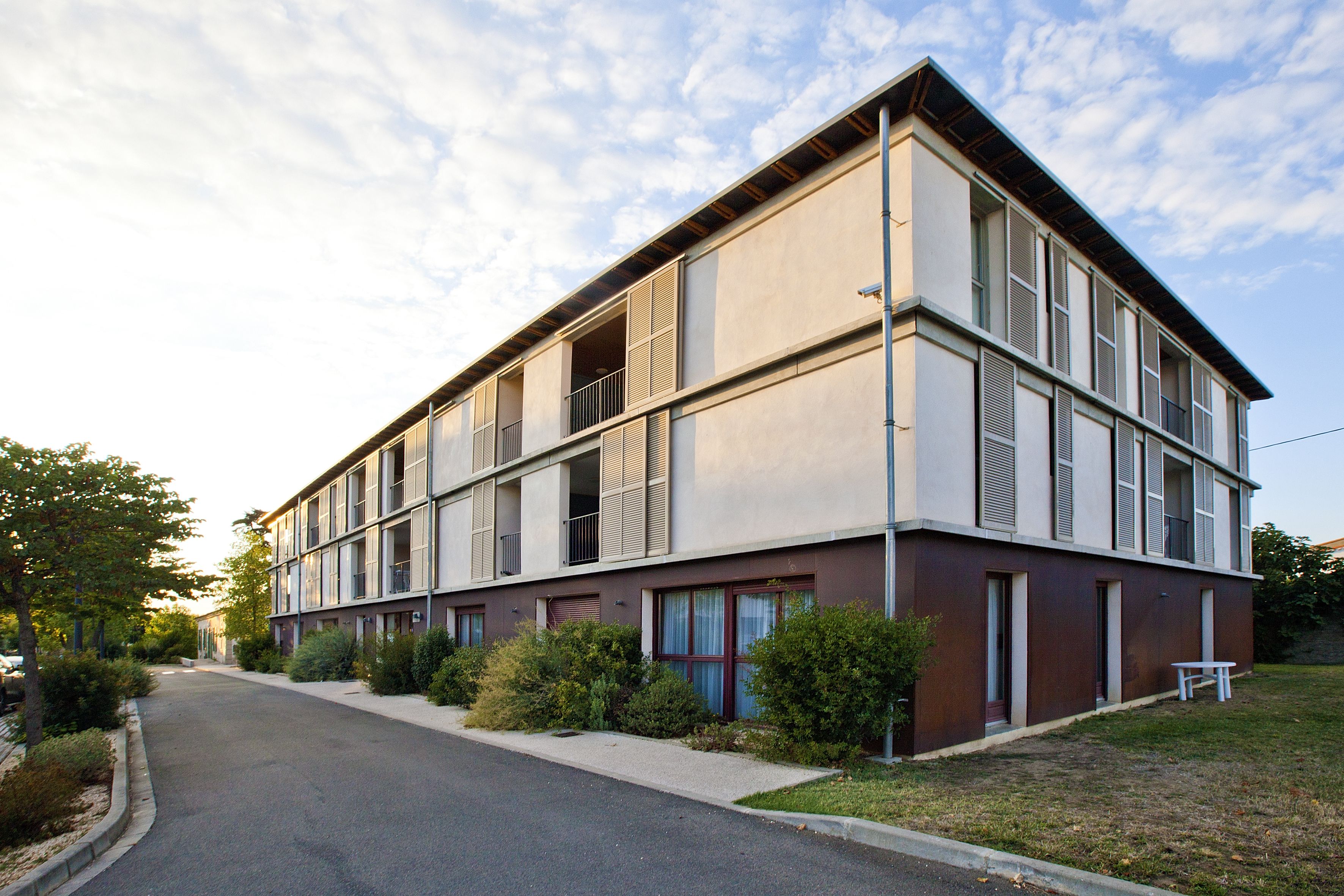 A modern multi-story building with a flat roof, large windows, and a paved driveway.