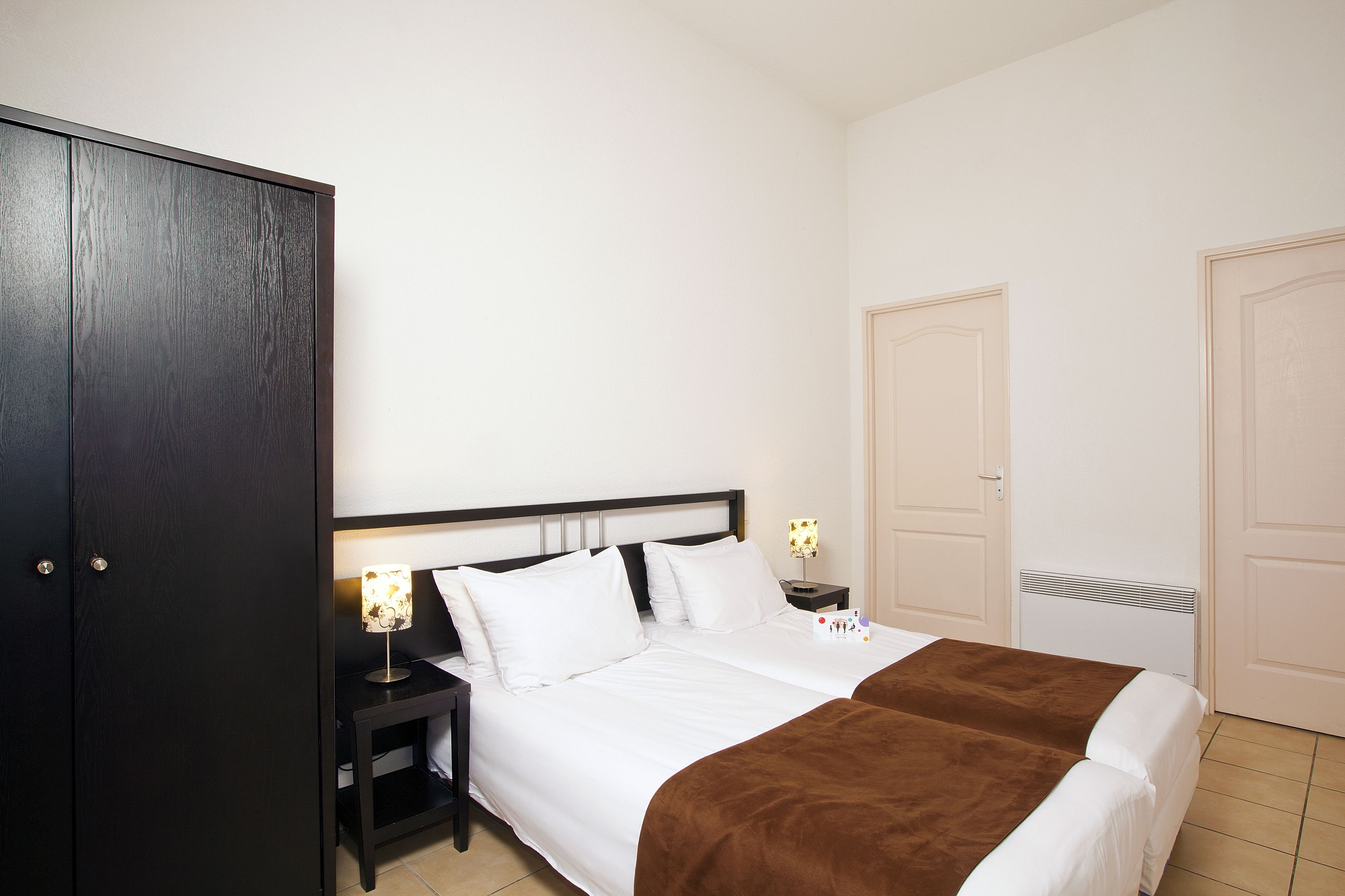 A hotel room with a bed, bedside tables, a wardrobe, and two doors.