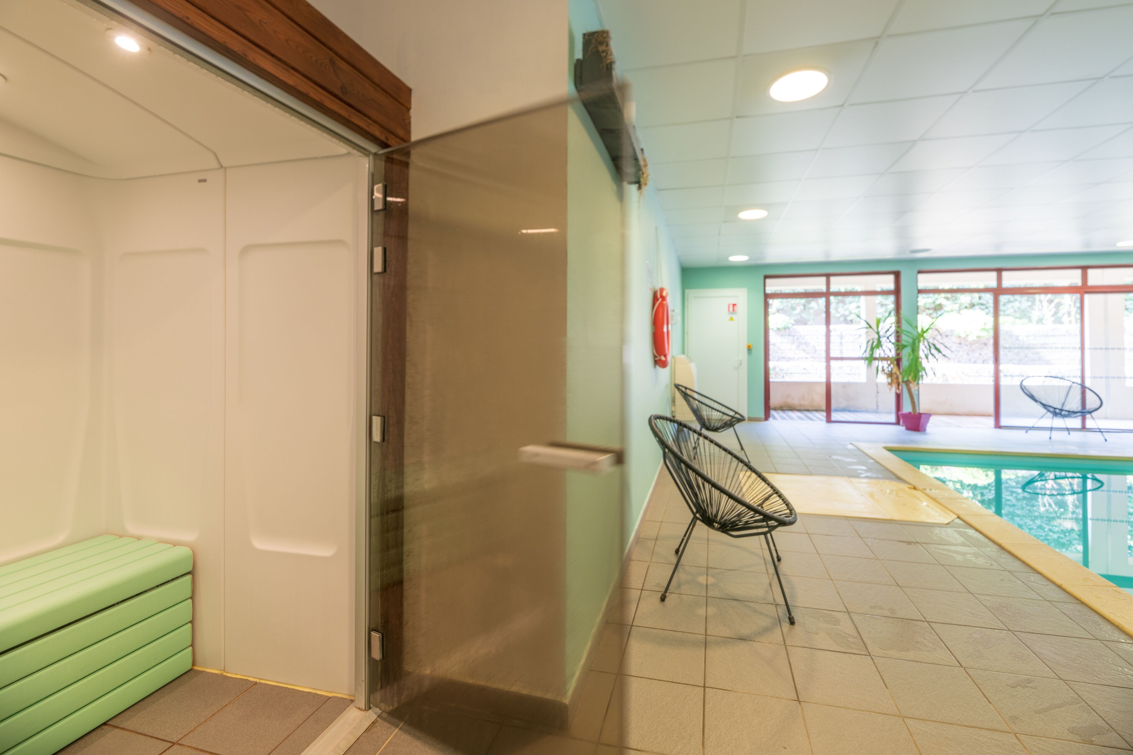 Une chambre d’hôtel avec un canapé vert, une porte en verre, un espace piscine avec des chaises et une plante en pot.