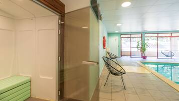 Une chambre d’hôtel avec un canapé vert, une porte en verre, un espace piscine avec des chaises et une plante en pot.