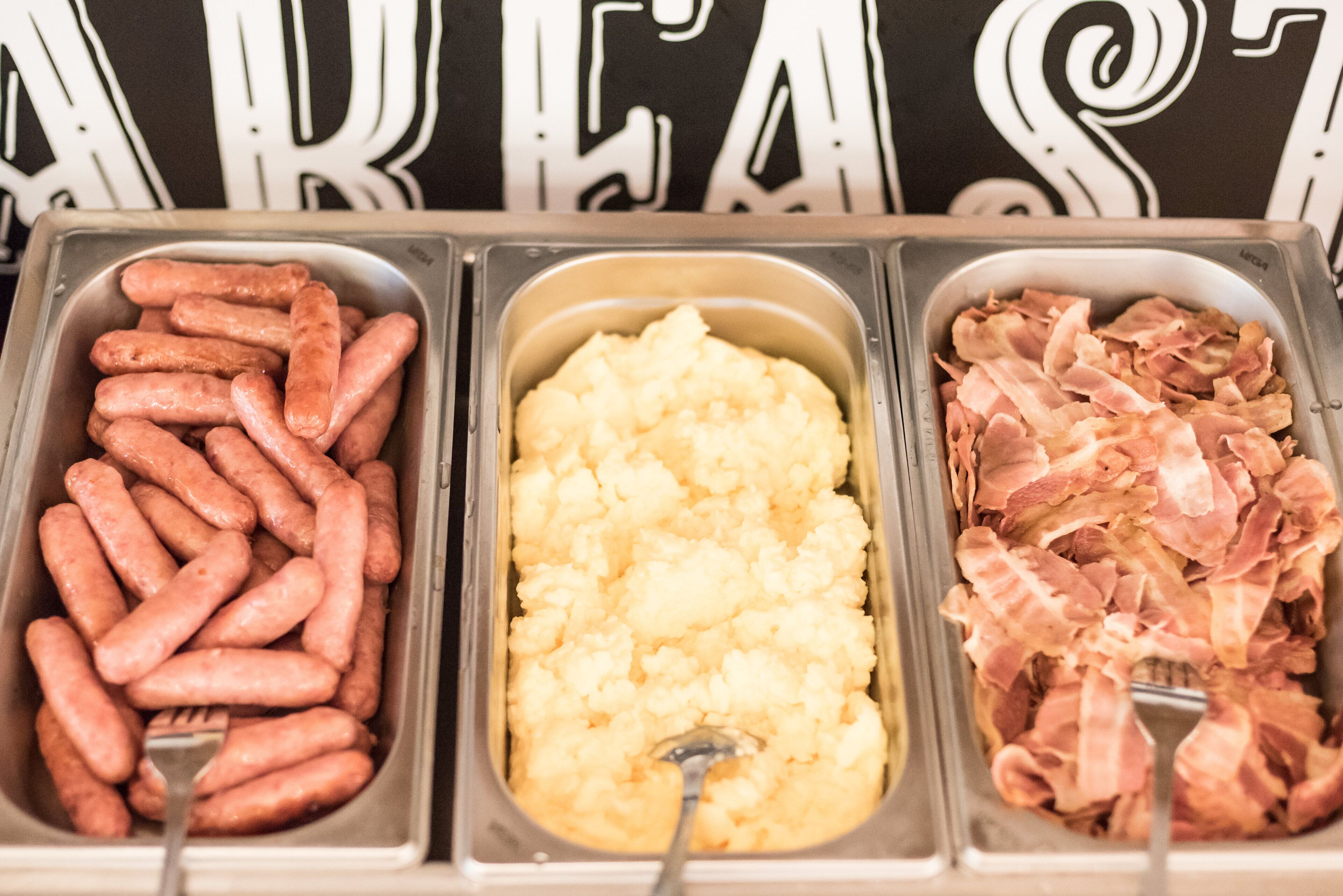 Três distribuidores de comida com salsichas, purê de batatas e bacon.