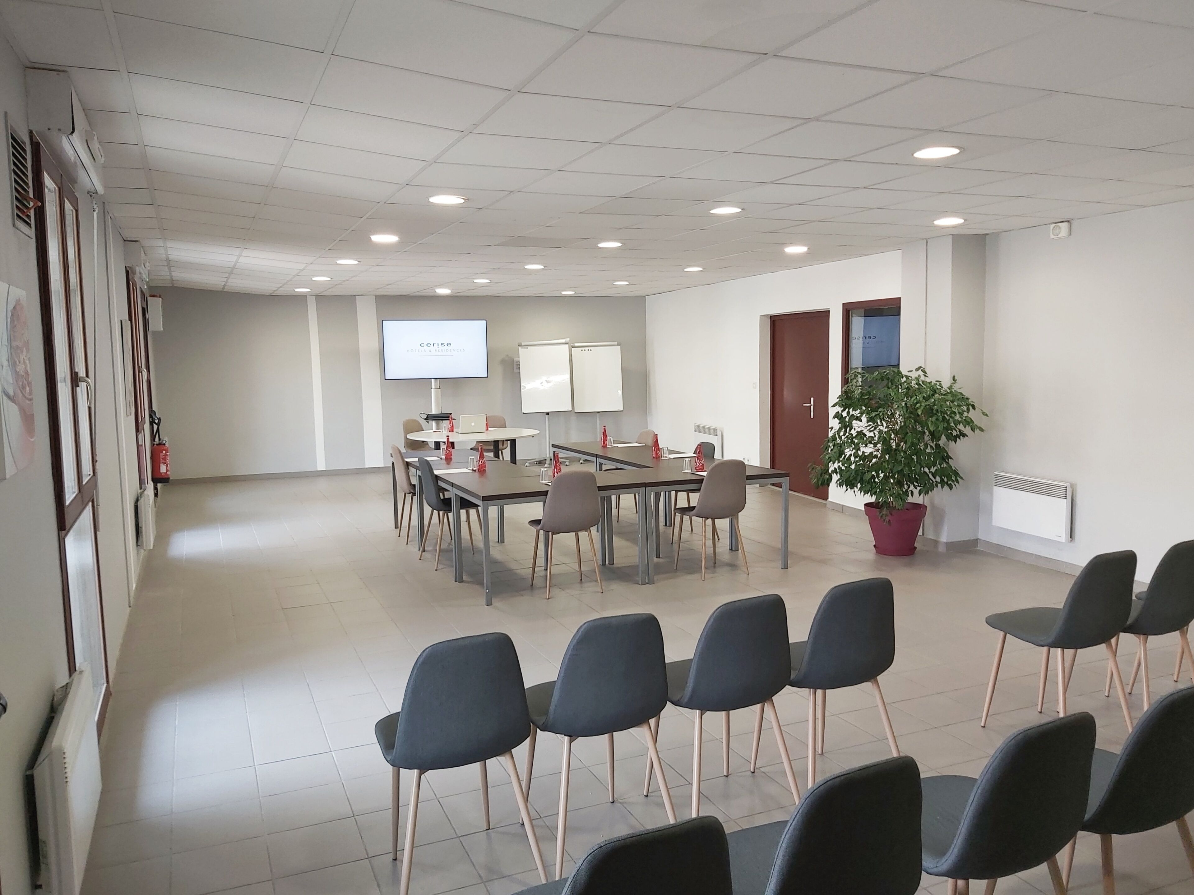Una sala conferenze con un tavolo grande, sedie, uno schermo per proiettore, lavagne e una pianta in vaso.