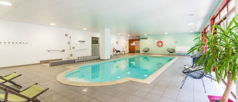 Una piscina interior con suelo de baldosas, sillas de descanso y una planta en maceta.