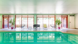 Una piscina con interior iluminado por el sol, rodeada de amplias ventanas y plantas en macetas.