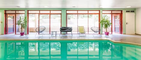 A swimming pool with a sunlit interior, surrounded by large windows and potted plants.