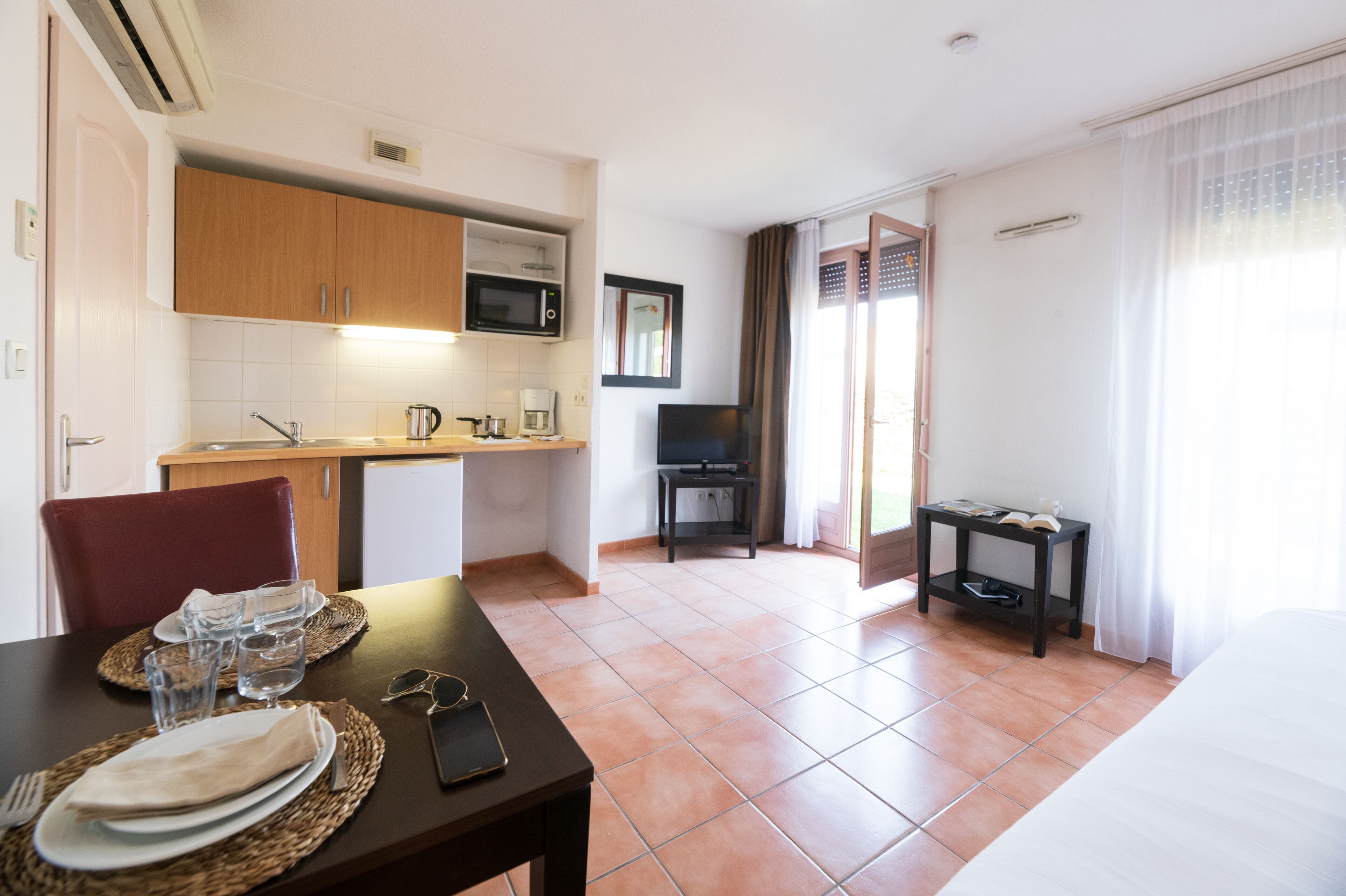 A compact hotel room with a kitchenette, a dining area, a TV, and a bed.