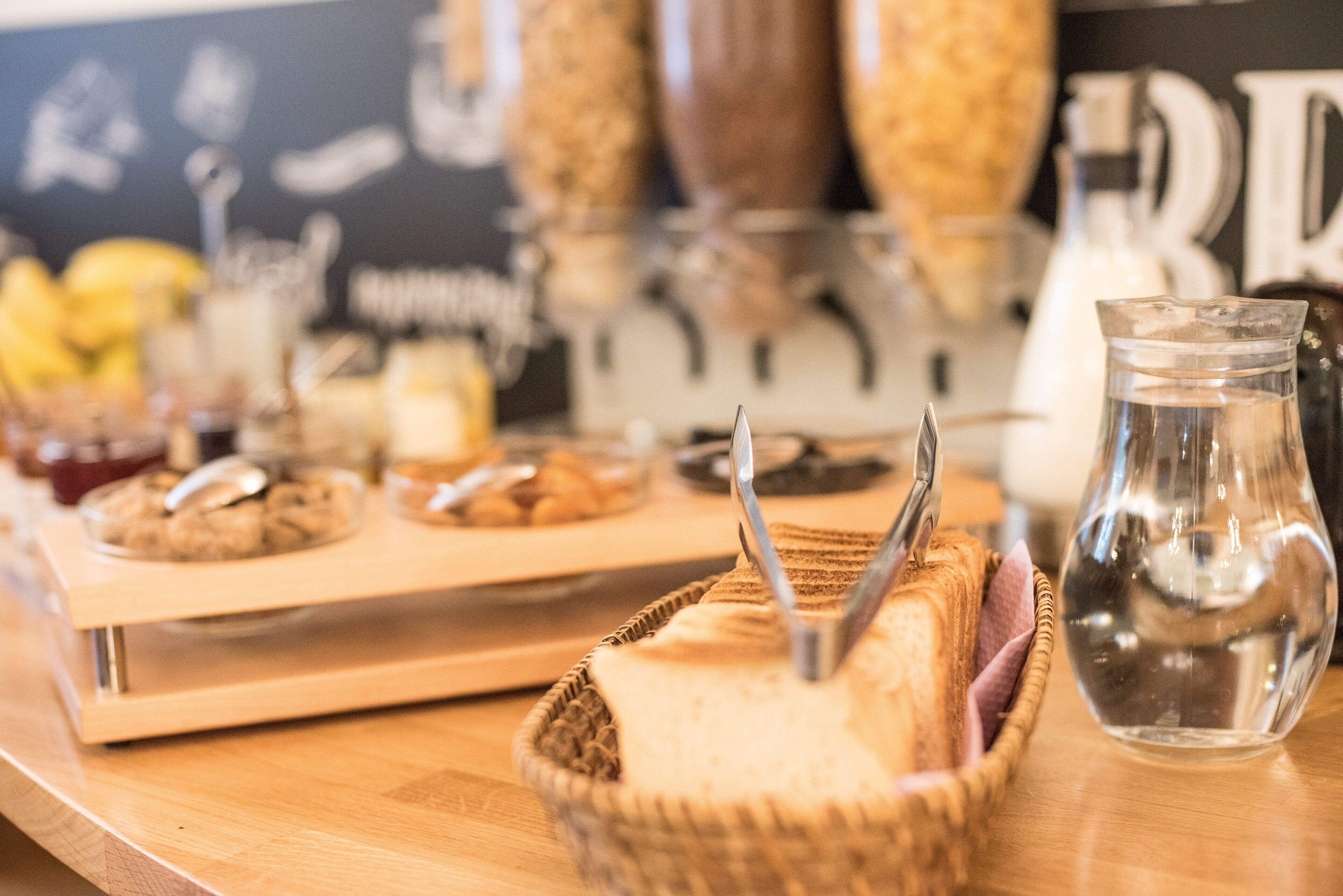 Una mesa de madera con una cesta de pan, una jarra de vidrio y una bandeja de galletas.