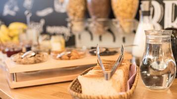 Una mesa de madera con una cesta de pan, una jarra de vidrio y una bandeja de galletas.