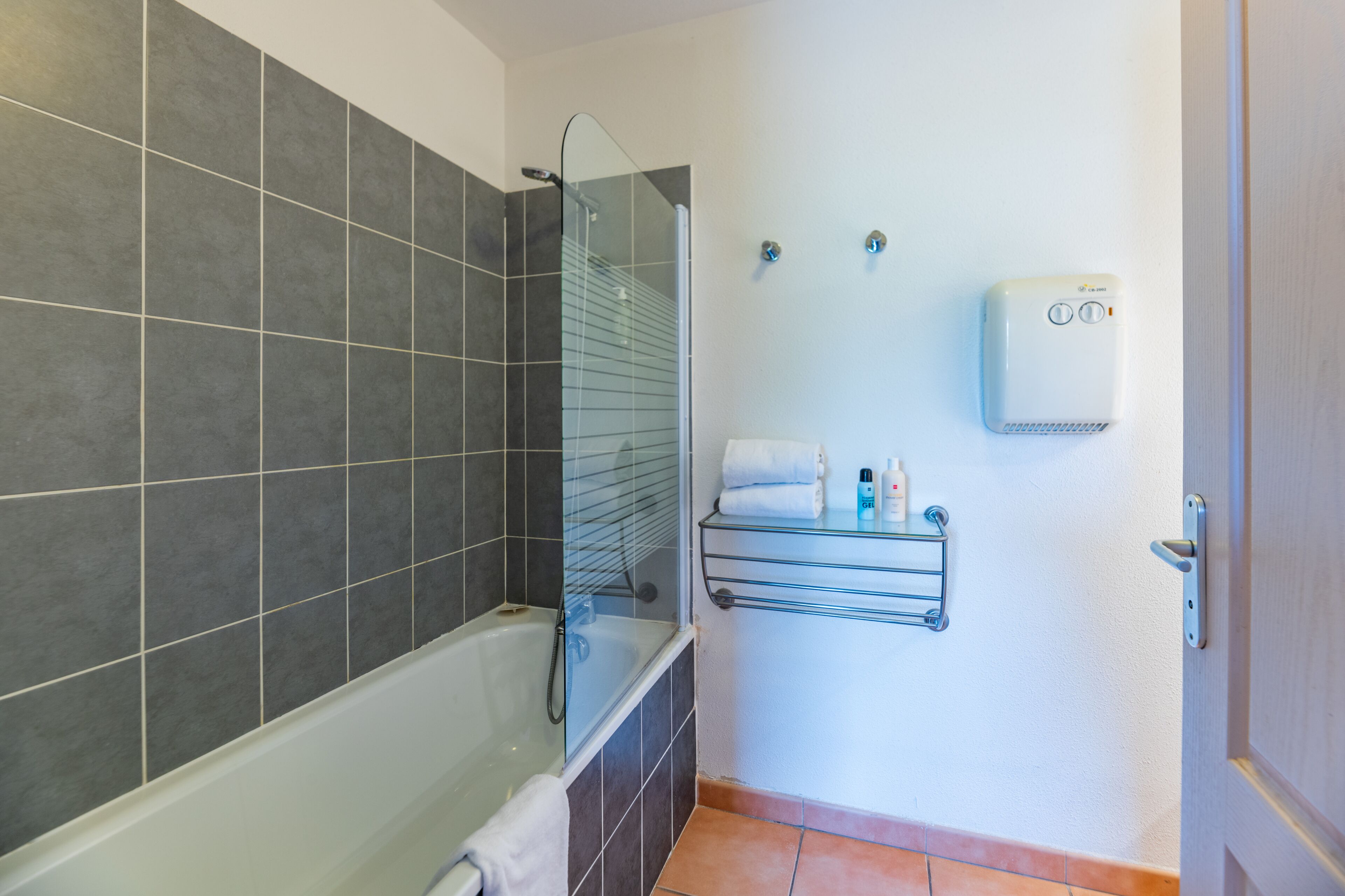 A modern bathroom with a glass-enclosed shower, a built-in towel rack, and a wall-mounted hand dryer.