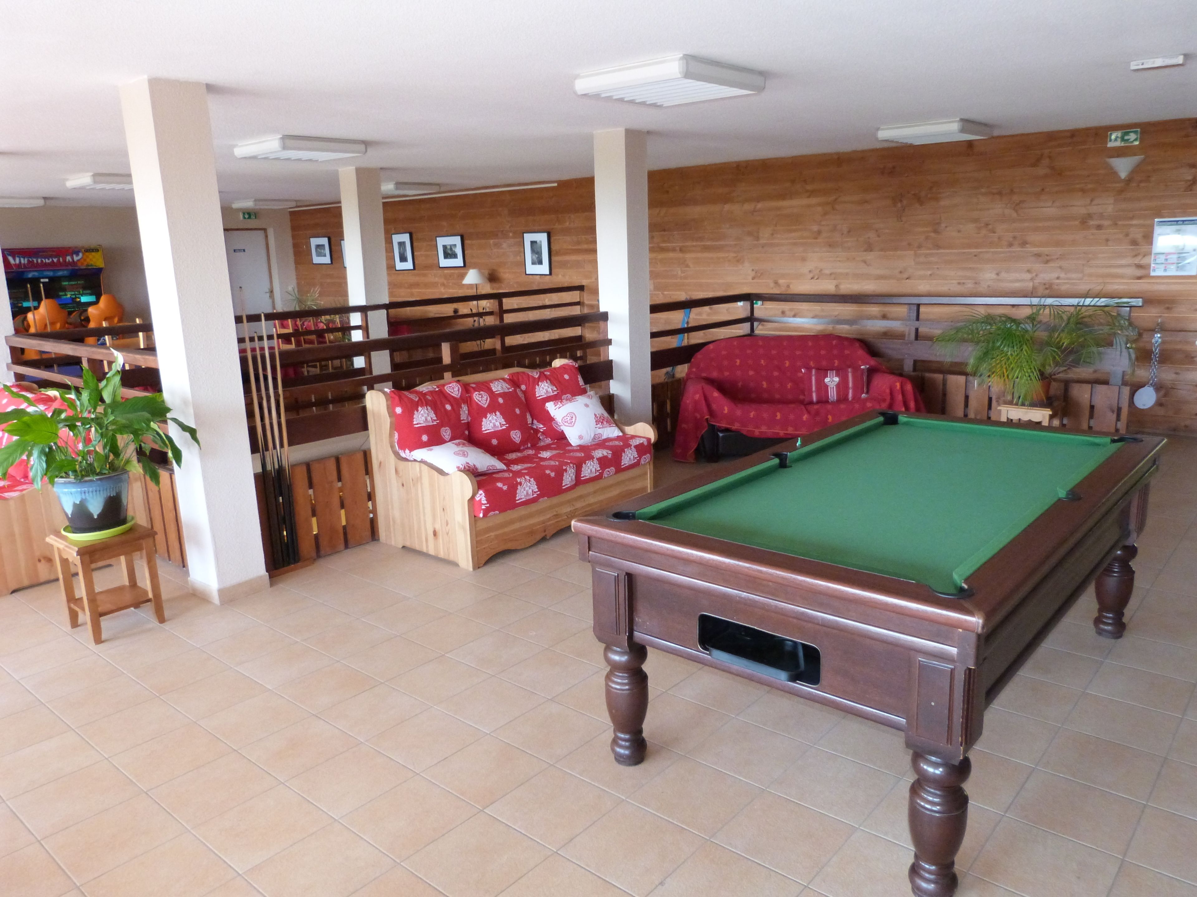 Une table de billard dans une pièce où se trouvent un banc en bois et un canapé rouge.