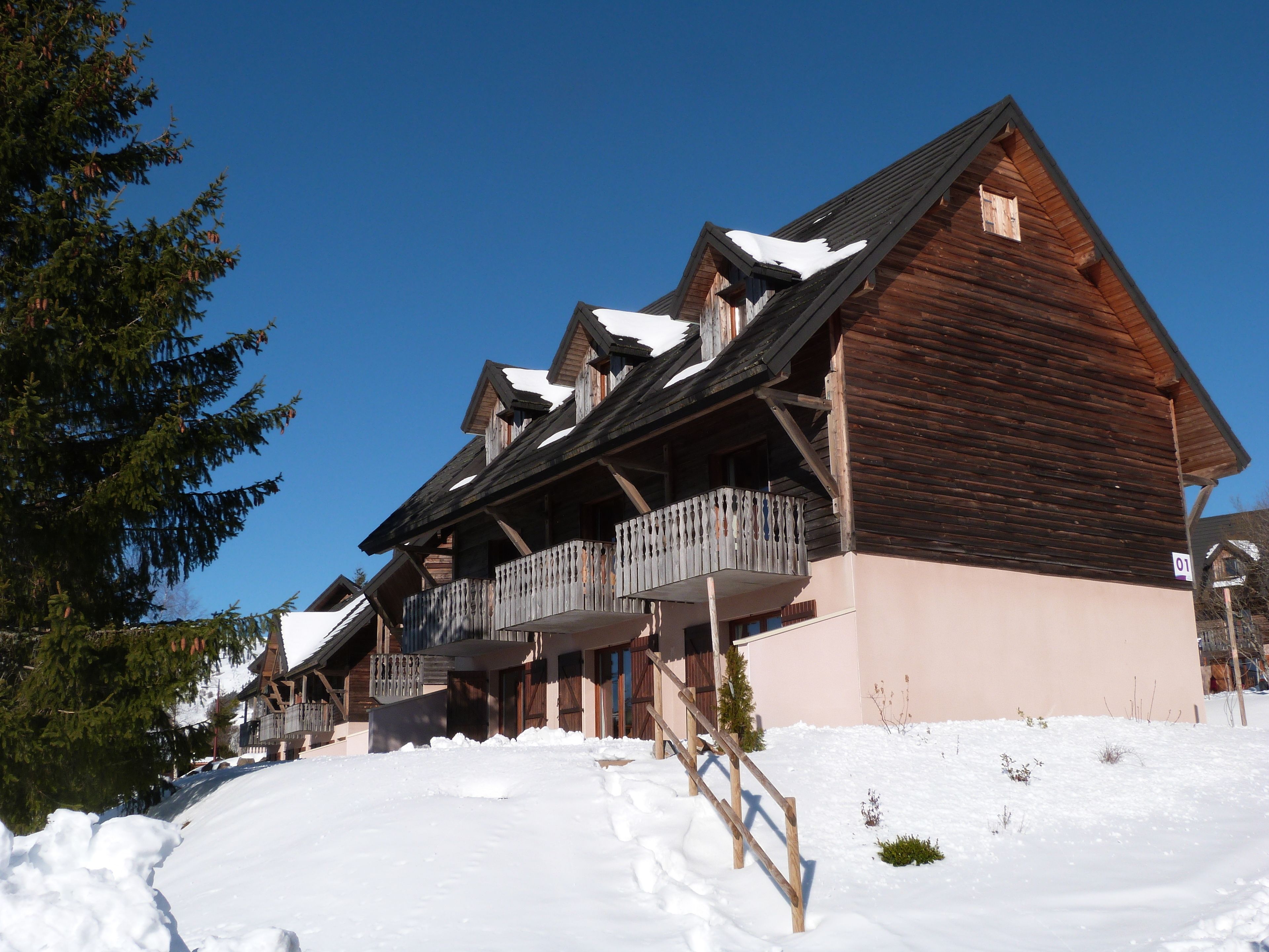 A wooden chalet with multiple balconies, a sloped roof, and a snow-covered ground.