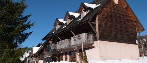 A wooden chalet with multiple balconies, a sloped roof, and a snow-covered ground.