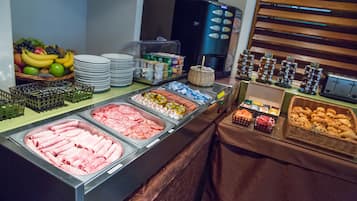 A buffet with various food options including meats, fruits, and pastries.