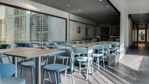 Un espace repas moderne, doté de tables et de chaises, de grandes fenêtres et d’un plafond orné de motifs.