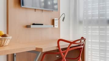 A modern room with a wooden desk, a red chair, a mounted TV, and a window with sheer curtains.