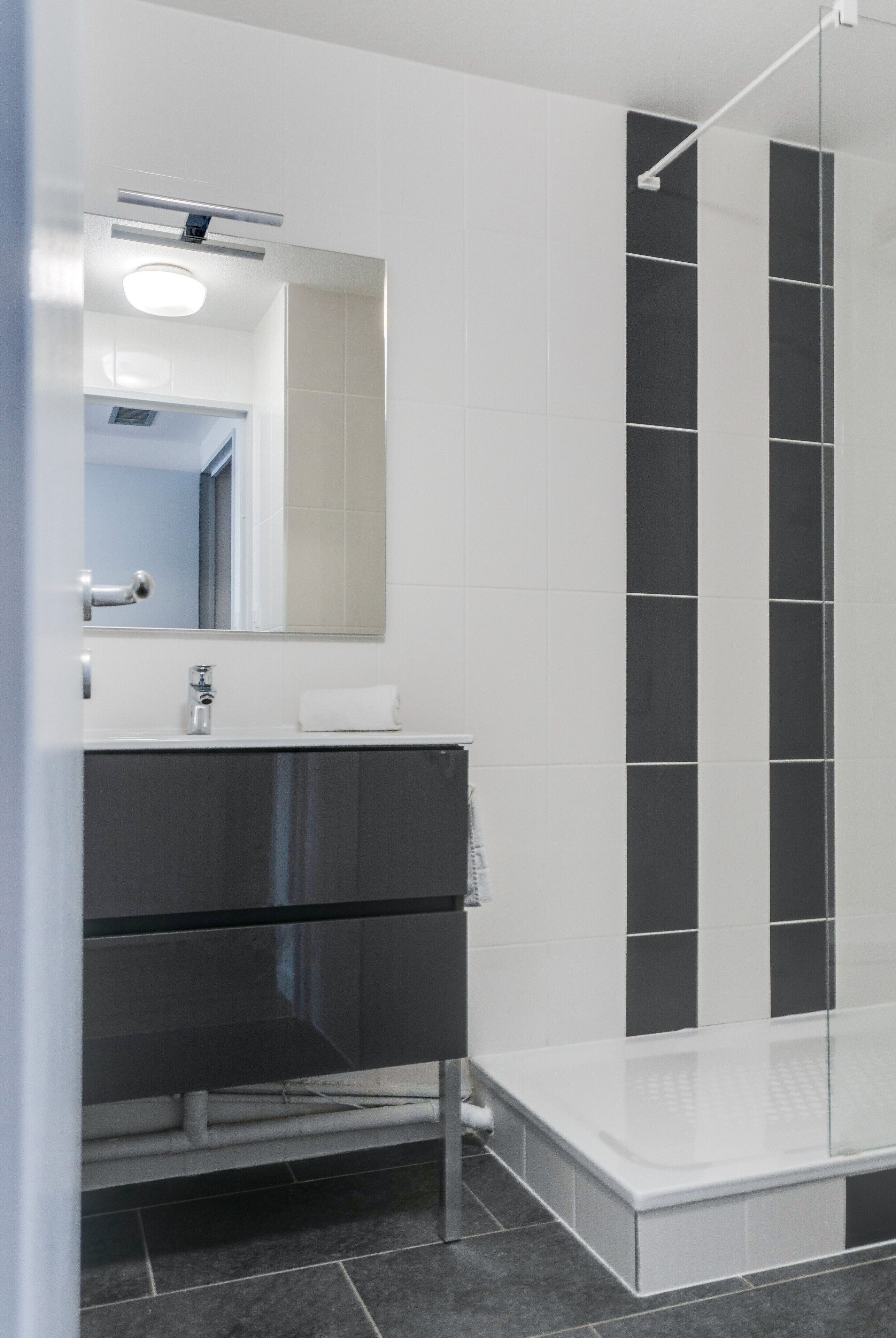 A modern bathroom with a glass shower enclosure, a large mirror, and a dark-colored vanity.