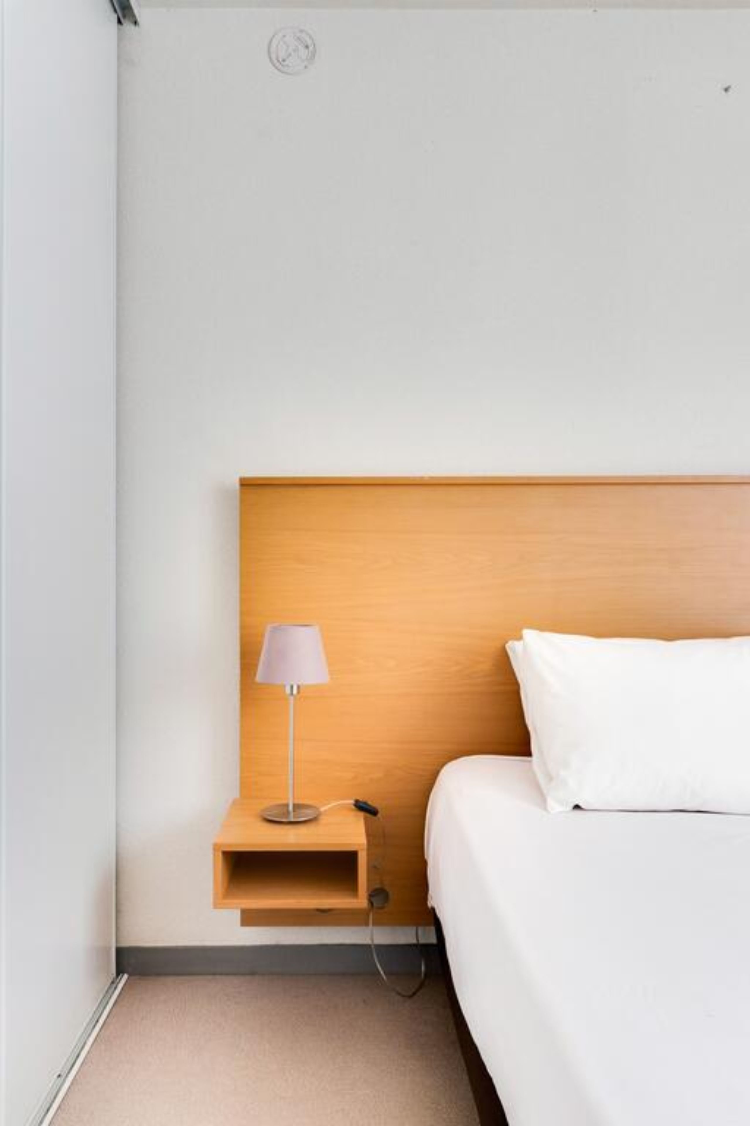 Une chambre d’hôtel avec une tête de lit en bois, une table de chevet avec une lampe et un lit blanc.