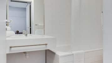 Un baño con lavamanos, espejo y bañera blancos.